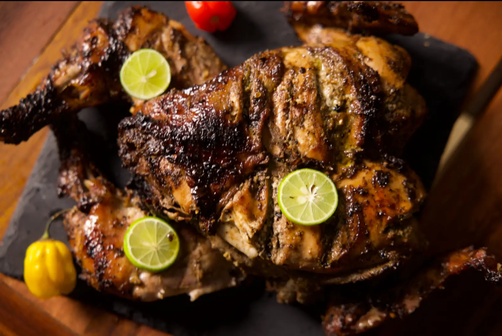Jerk chicken searing over glowing charcoal with scotch bonnet peppers and lime